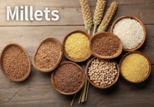 Various types of raw millets like Ragi, Jowar, and Bajra in wooden bowls with millet stalks on a rustic wooden background.